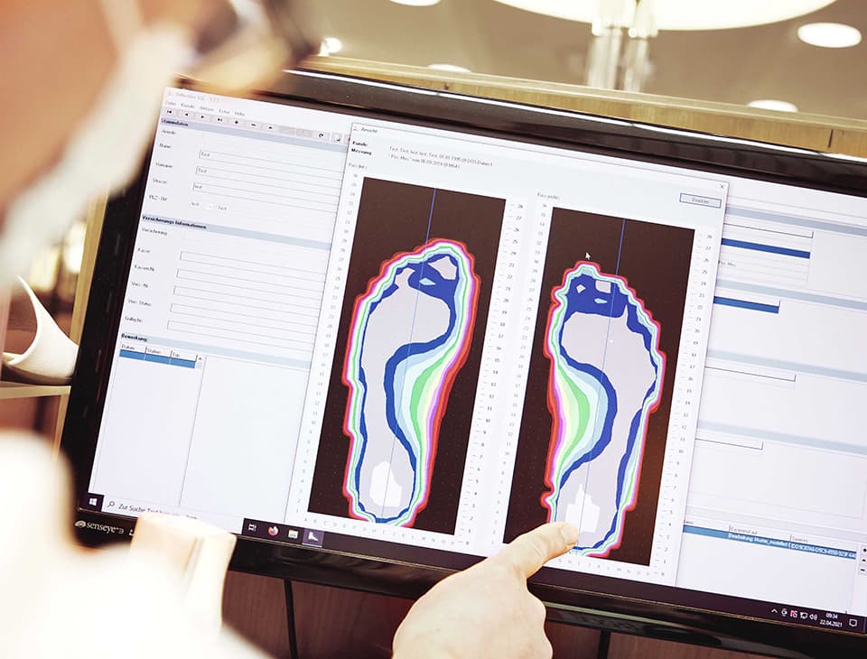 A person points at a computer screen displaying a detailed foot pressure analysis with colorful contours and graphs.